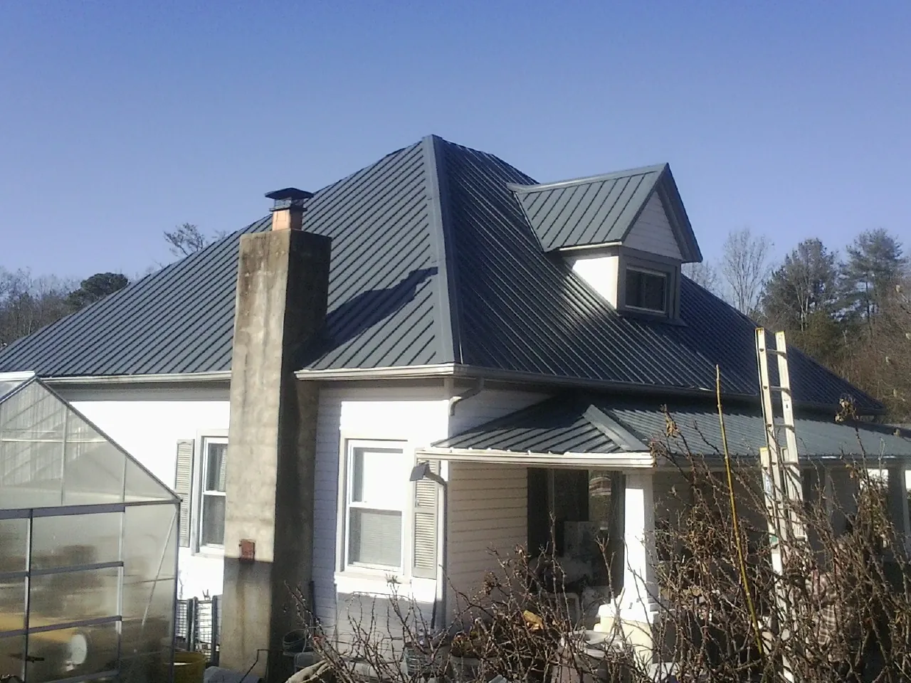 Dark blue standing seam metal roof on a white farmhouse with dormer — Slate & Tile Roof Repair by Roofing Brothers in Mottville