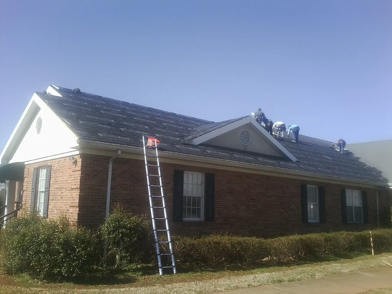 Crew tearing shingles off a brick ranch roof with a ladder set — Metal Roof Repair work by our crew in Mottville