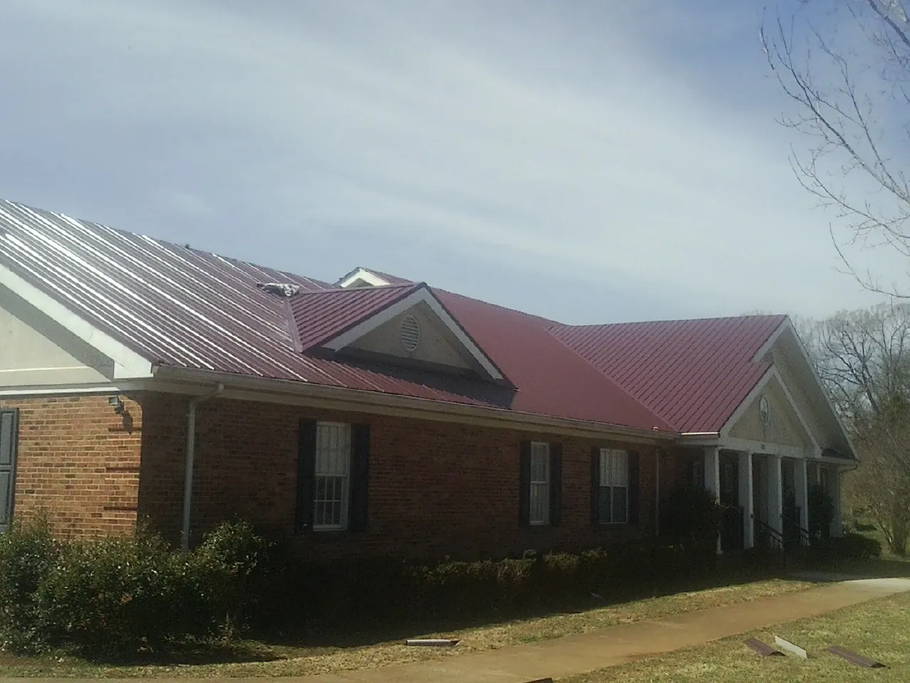 Red metal roof with gabled entries on a long brick building, from a Hail Damage Roof Repair job in Mottville