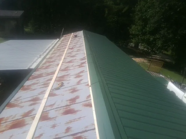 Old rusted panels beside newly installed green metal roofing — Wind Damage Roof Repair by Roofing Brothers in Mottville