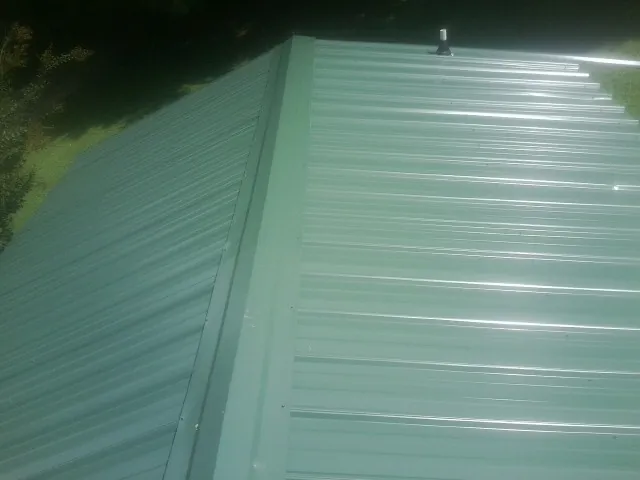 New green metal panels meeting at the ridge of a roof — Flat Roof Repair work by our crew in Mottville