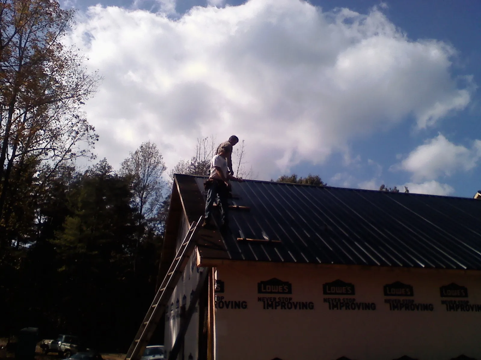 Roofer fastening dark metal panels high against a cloudy sky, from a Roof Inspection job in Mottville