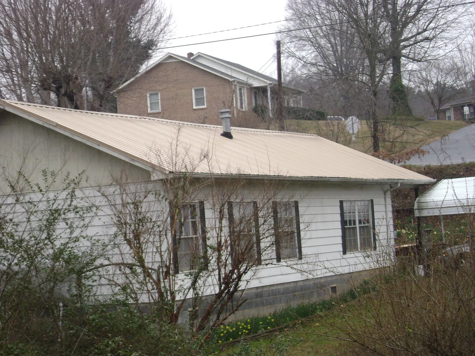 Tan metal roof on a white sided house set into a hillside — Commercial Roofing by Roofing Brothers in Mottville