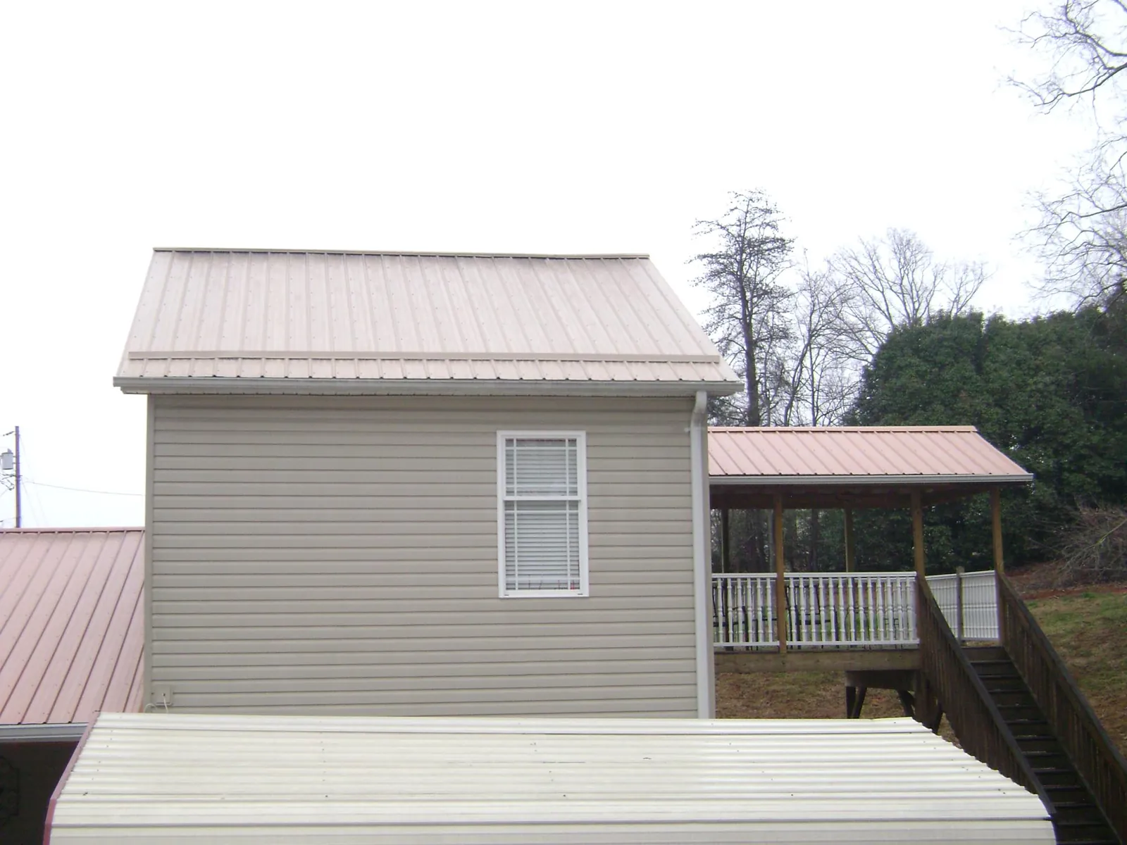 Tan metal roofs on a two story addition and attached porch, from a Roof Replacement job in Mottville